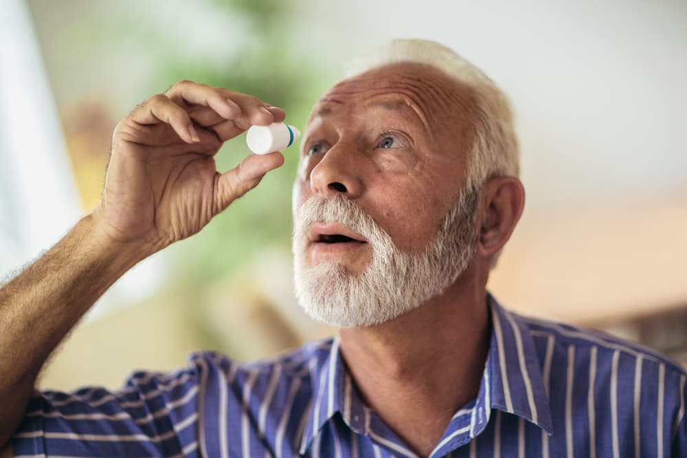 Older man putting eye drops in his eye